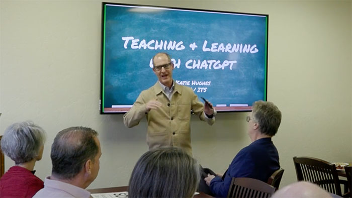 Instructor gestures while presenting to faculty during a session titled “Teaching and Learning with ChatGPT,” displayed on a screen.